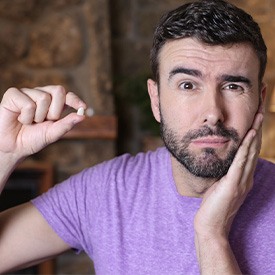 Man in purple shirt holding tooth in one hand and hand to jaw with the other