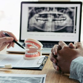 Dentist’s and patient’s hands at desk going over X-rays and model teeth