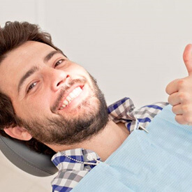 dental patient reclining in treatment chair, making thumbs-up gesture