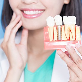 Dentist holding her jaw with one hand and a model dental implant in the other