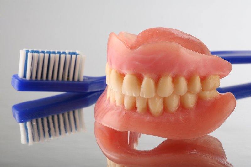 Full dentures sitting next to a soft-bristled toothbrush